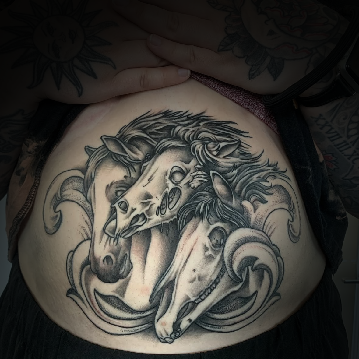 Black and grey Tattoo of three horse heads on a person's stomach area by Dominic, tattoo artist at Sundog Studios in Airdrie Alberta