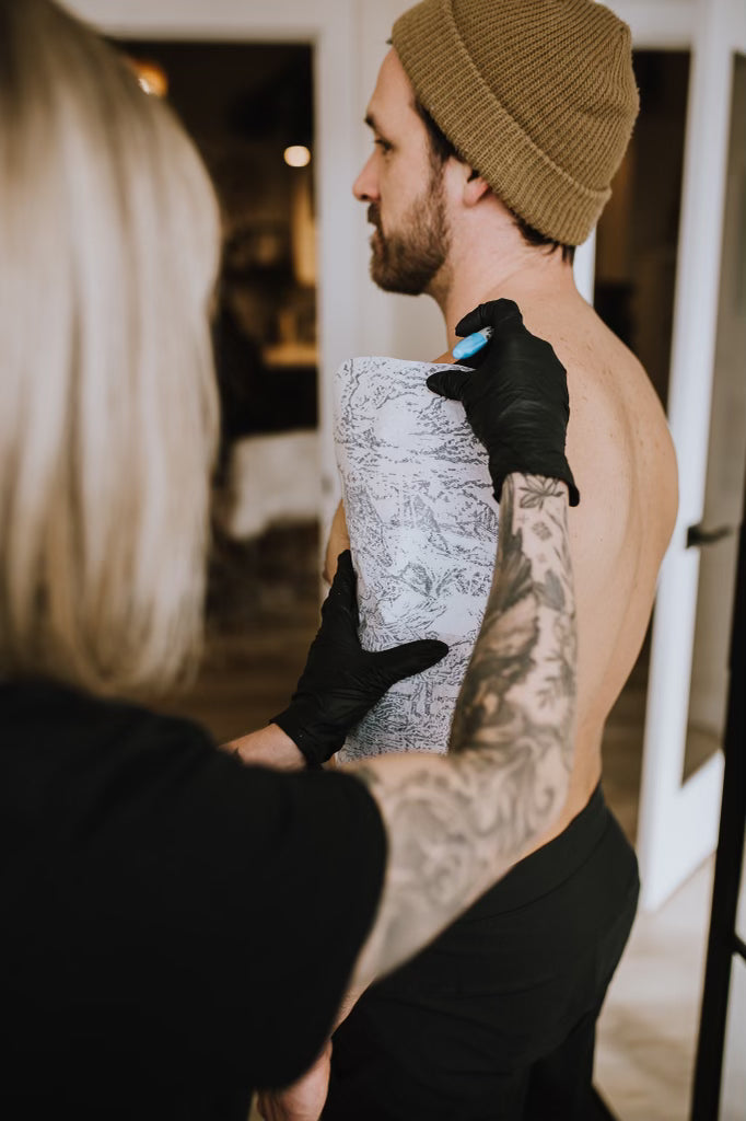 tattoo artist placing stencil on client's upper back at Sundog Studios tattoo shop in Airdrie, Alberta