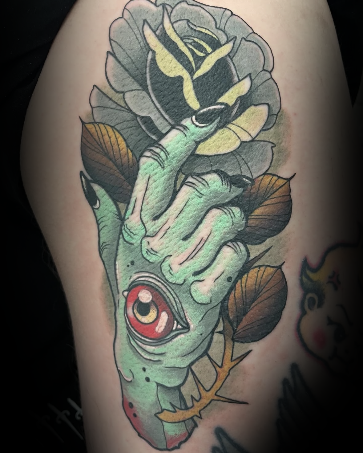 Colour tattoo of a green hand with red eye and black flower and thorns by Rob Adams, tattoo artist at Sundog Studios in Airdrie Alberta