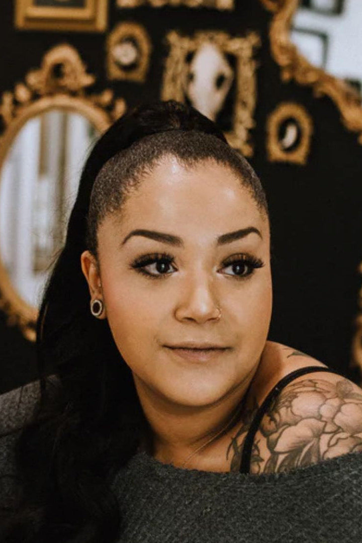 Professional Tattoo Artist in Airdrie Sundog Studios, Mahala with tattoos sitting in front of decorative mirrors