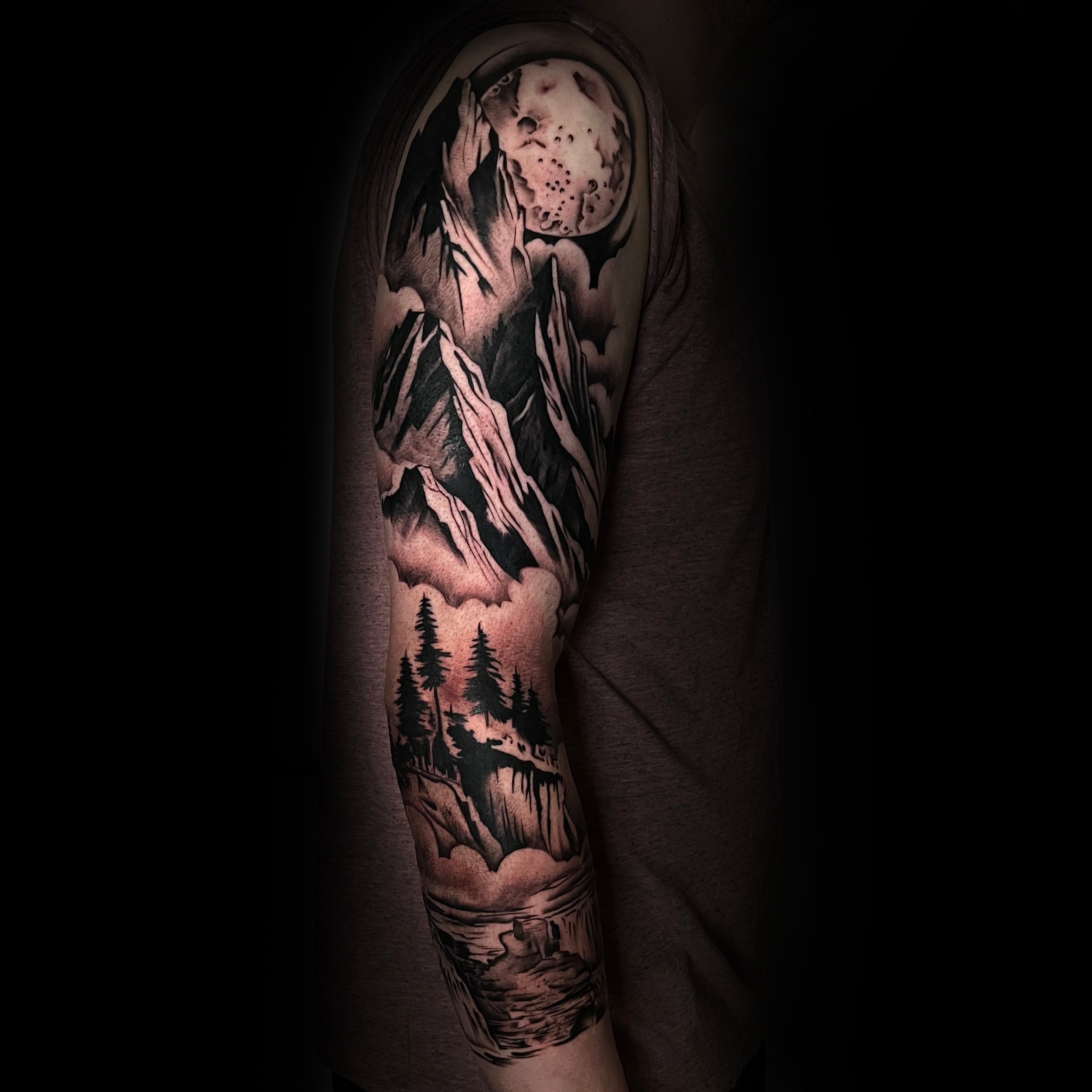 Tattoo sleeve of a mountain landscape with moon on top and river and trees on lower part by Dominic, tattoo artist at Sundog Studios in Airdrie Alberta