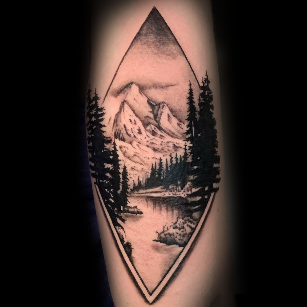 Tattoo of a mountain landscape with trees and a lake inside an eye shape by Dominic, tattoo artist at Sundog Studios in Airdrie Alberta