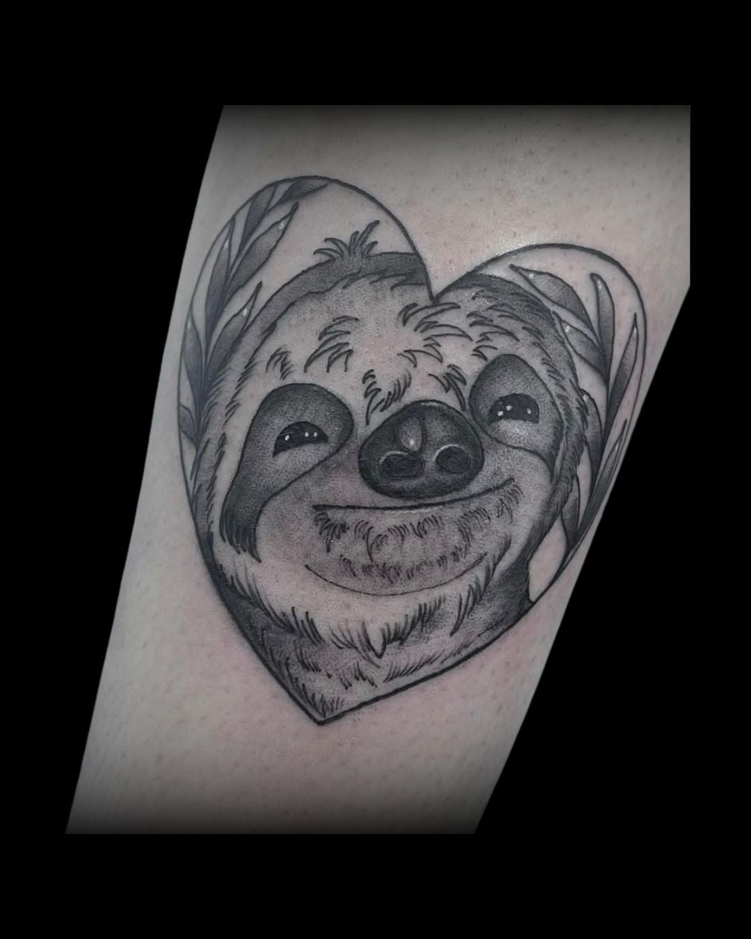 Black and gray tattoo of a sloth's face on a heart-shaped by Mahala, tattoo artist at Sundog Studios in Airdrie Alberta