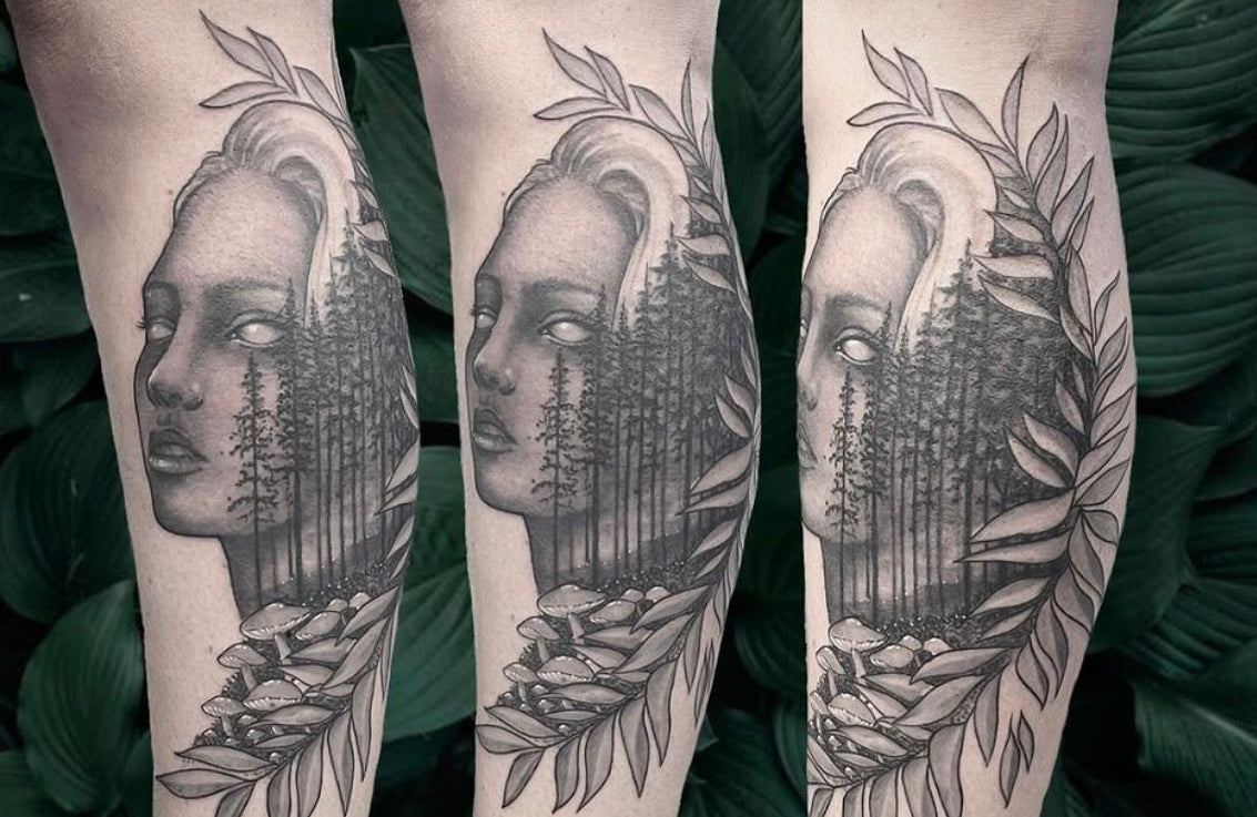 Black and grey realism tattoo of a woman's face with pine trees and botanical leaves, created by a Sundog Studios tattoo artist in Airdrie Alberta